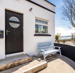 An exterior entrance with a black door and a window next to a light blue bench by a curved wall at The Old Coastguard Tower Buncrana County Donegal