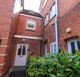 A brick building entrance with a white door and green plants nearby at The Lobster Pot in Weymouth