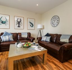 A living room with two brown leather sofas a coffee table with fruit and tea set and wall art at The Lobster Pot in Weymouth