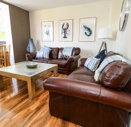 A living room with brown leather sofas a wooden coffee table and framed pictures of sea creatures on the wall at The Lobster Pot in Weymouth