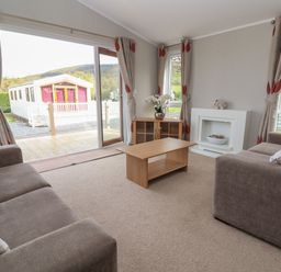 A living room with two sofas a coffee table a cabinet and a sliding glass door at Lodge 4 in St Asaph