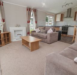 A living room with sofas coffee table wooden cabinet and kitchen in the background at Lodge 4 in St Asaph