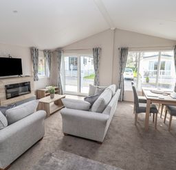 A living room with two grey sofas a wooden coffee table a wall mounted TV and a dining table with four chairs at Lodge 9 in St Asaph