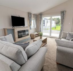A living room with two light grey sofas a wooden coffee table and a TV on a wooden stand with an electric fireplace at Lodge 9 in St Asaph