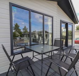 An outdoor patio with a glass table and four black chairs outside a house at Lodge 9 in St Asaph