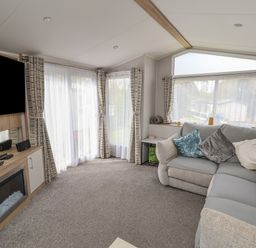 A living room with a sectional sofa cushions curtains and a TV above a fireplace at Woodlands Lodge in Bontuchel near Ruthin
