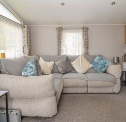 A living room with a patterned sofa and multiple cushions near windows with curtains at Woodlands Lodge in Bontuchel near Ruthin