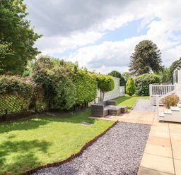 An outdoor area with patio flooring seating and grass next to white mobile homes at Woodlands Lodge in Bontuchel near Ruthin