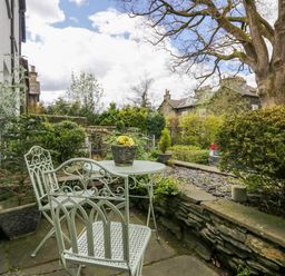 An outdoor patio area with metal table and chairs surrounded by plants and stone walls at Acorn Cottage in Windermere