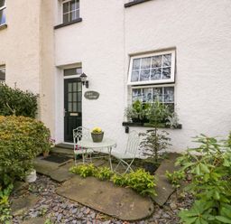 The exterior of a house with a black door a window with plants on the sill a round metal table with two chairs and plants in front at Acorn Cottage in Windermere