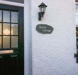 A front door with glass panels next to a wall lamp and a sign reading Acorn Cottage at Acorn Cottage in Windermere