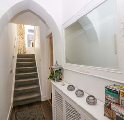 A hallway with carpeted stairs under an arched ceiling a large framed mirror and a white radiator cover with decorative items at Acorn Cottage in Windermere