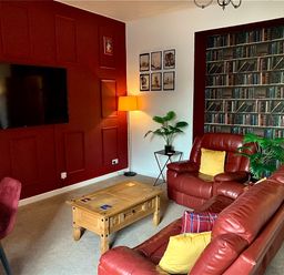A living room with red leather sofas wooden coffee table plants and a television mounted on a red wall at The Wizard's Chamber in Alnwick