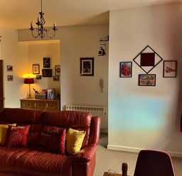 A living room with a leather sofa pillows wall art and a wooden cabinet with a lamp at The Wizard's Chamber in Alnwick