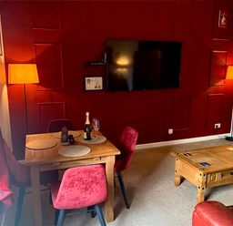 A dining area with a wooden table and four red chairs next to a wall with a mounted TV and two floor lamps at The Wizard's Chamber in Alnwick