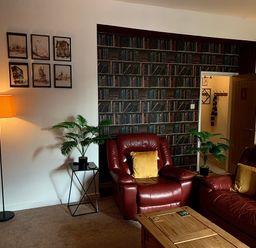 A room with red leather chairs and sofa a wooden coffee table plants a floor lamp framed pictures and books wallpaper at The Wizard's Chamber in Alnwick