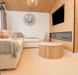 A living room with a white sectional sofa colorful cushions a round wooden coffee table a wall-mounted TV and a modern fireplace at Encil Gyfrinfa in Gwynus near Llithfaen