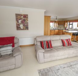 A living room with gray sofas red and gray pillows a red throw a painting of flowers on the wall and a kitchen with wooden cabinets and bar stools in the background at Bunny Lane in Cloonflynn near Ballycarra County Mayo