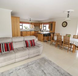 An open living area with a beige sofa with red striped cushions a wooden dining table with chairs and a kitchen with wooden cabinets and bar stools at Bunny Lane in Cloonflynn near Ballycarra County Mayo