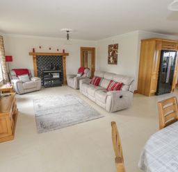 A living room with gray sofas and armchairs a black wood-burning stove wooden cabinets and a dining table at Bunny Lane in Cloonflynn near Ballycarra County Mayo