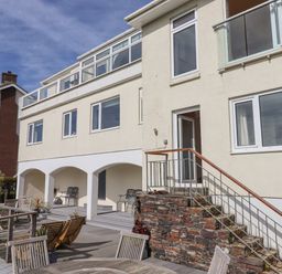 An outdoor decking area with wooden tables and chairs in front of a multi-story building with arches and multiple windows at Seahaze in Downderry