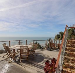 An outdoor wooden deck with a round table and six chairs overlooking the sea at Seahaze in Downderry