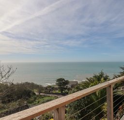 A view of the ocean from a balcony with a wooden railing and trees below at Seahaze in Downderry