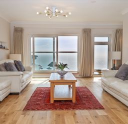 A living room with two white sofas a wooden coffee table a red rug and large windows overlooking the sea at Seahaze in Downderry