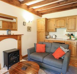 A living room with a sofa and kitchen area at Royal Oak Farm Cottage in Betws-y-Coed
