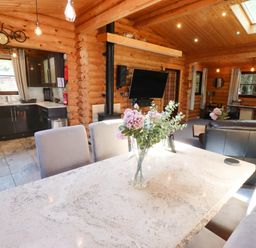 An open plan living and kitchen area with dining table and chairs a television and a sofa in a wooden cabin at Starwood in Felton