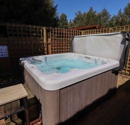 An outdoor hot tub with water inside and a cover partially open surrounded by wooden lattice fencing at Starwood in Felton