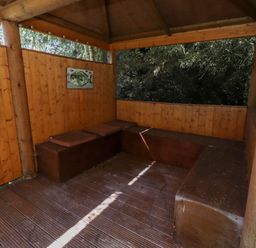 A wooden gazebo with built-in benches and cushions surrounded by trees at Starwood Felton