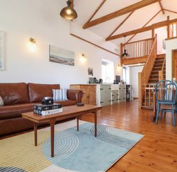 An open living area with a brown leather sofa a wooden coffee table and a kitchen in the background at Joes Barn in Mullion