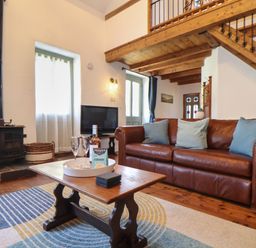 A living room with a leather sofa coffee table with wine and glasses wood stove and staircase at Berts Barn in Mullion