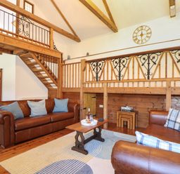 A living room with brown leather sofas a wooden coffee table and a staircase with wooden and metal railing at Berts Barn in Mullion