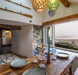 A dining area with a wooden table set with plates and glasses next to a window overlooking a coastal view at Pengarreg in Barmouth
