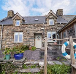 Stone house with gray door and windows flower pots and wooden deck with life buoy at Pengarreg in Barmouth