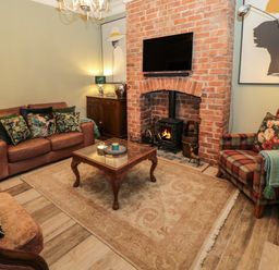 A living room with a wood stove in a brick fireplace a leather sofa a plaid armchair and a wooden coffee table at Sunflowers in Earsdon near Whitley Bay