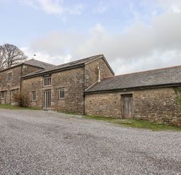 A stone barn with multiple windows and doors on a gravel driveway at Brimpts Barn Dartmeet near Princetown
