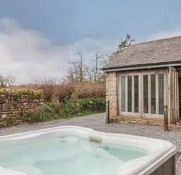 An outdoor hot tub next to a stone building with folding glass doors and a gravel ground at Brimpts Barn in Dartmeet near Princetown