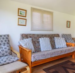 A living room with wooden framed seating and cushions with a window and framed pictures on the wall at Cornish Holiday at Atlantic Bays in St Merryn