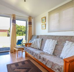 A living room with a sofa bed three cushions paintings on the wall and glass sliding doors at Cornish Holiday at Atlantic Bays in St Merryn