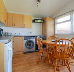 A kitchen with wooden cabinets a round wooden dining table and four chairs next to a large window at Cornish Holiday at Atlantic Bays in St Merryn