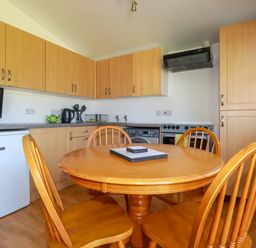 A kitchen with wooden cabinets a round wooden dining table with four chairs and kitchen appliances at Cornish Holiday at Atlantic Bays in St Merryn