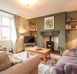A living room with sofas a wooden coffee table a fireplace a television and bookshelves at Lavender Cottage in Coniston