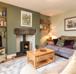 A living room with a fireplace a wooden coffee table sofas and bookshelves at Lavender Cottage in Coniston