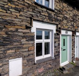 A stone cottage exterior with white framed windows and a green door at Lavender Cottage in Coniston