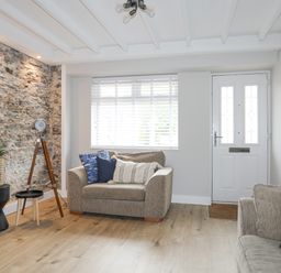 A living room with two sofas pillows a stone feature wall a tripod lamp and a white front door with windows at Ty Bara in Cemaes Bay