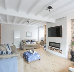 A living room with two sofas a blue patterned ottoman a wall mounted television and fireplace at Ty Bara in Cemaes Bay