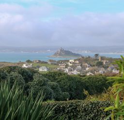 A coastal village with houses and greenery overlooking an island with a castle in the sea at An Skyber in Perranuthnoe